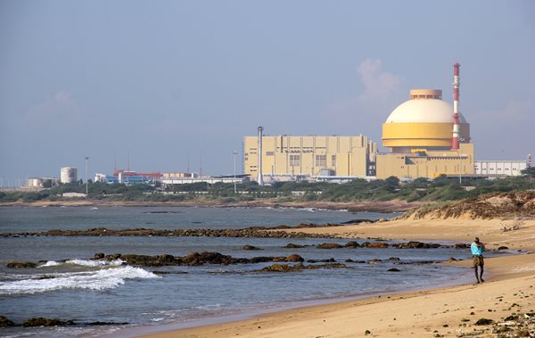 Man walks on beach in front of Kudankulam nuclear power plant, one of India's newest
